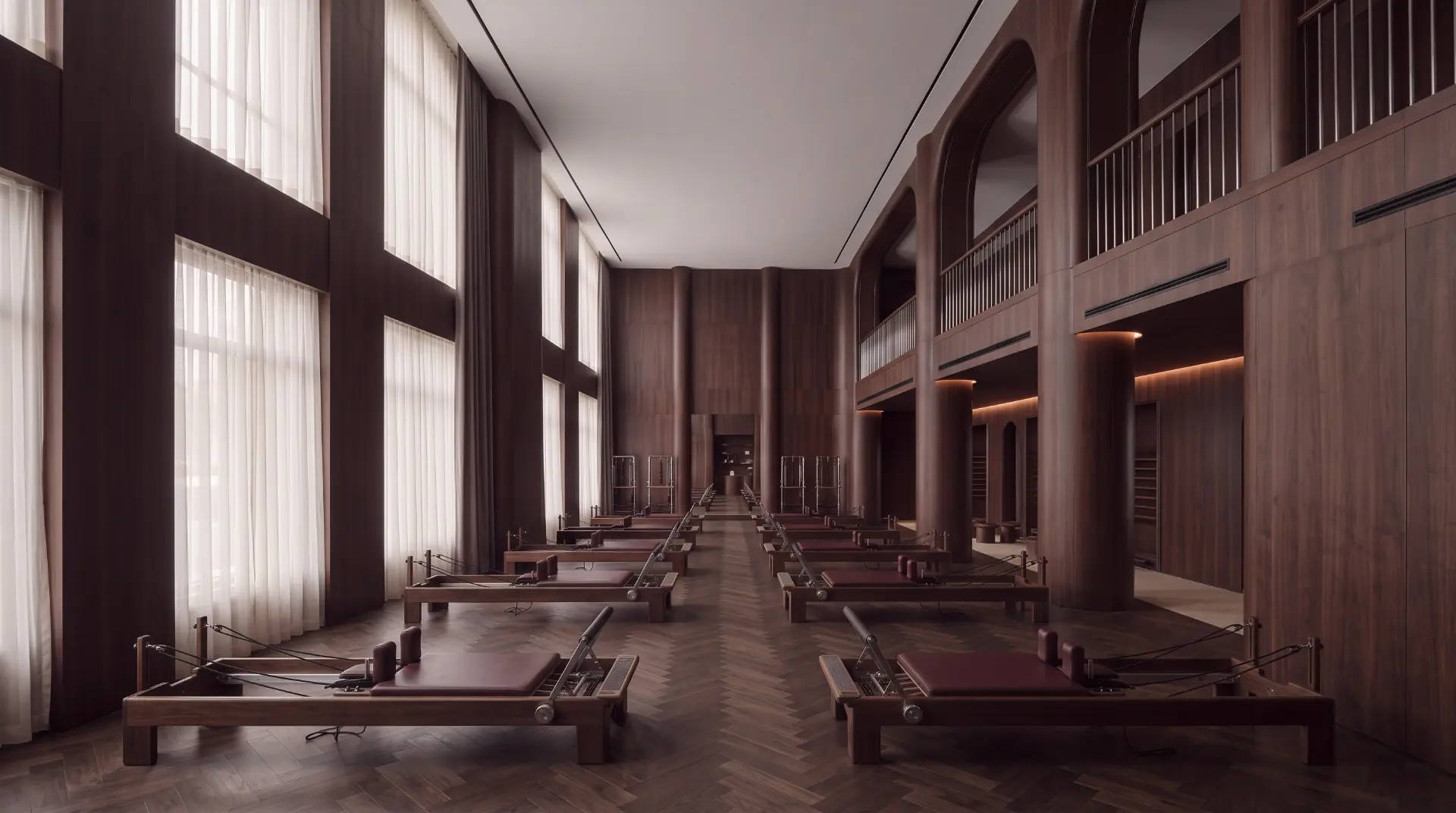 A walnut-panelled Pilates studio with reformer beds and tall curtained windows