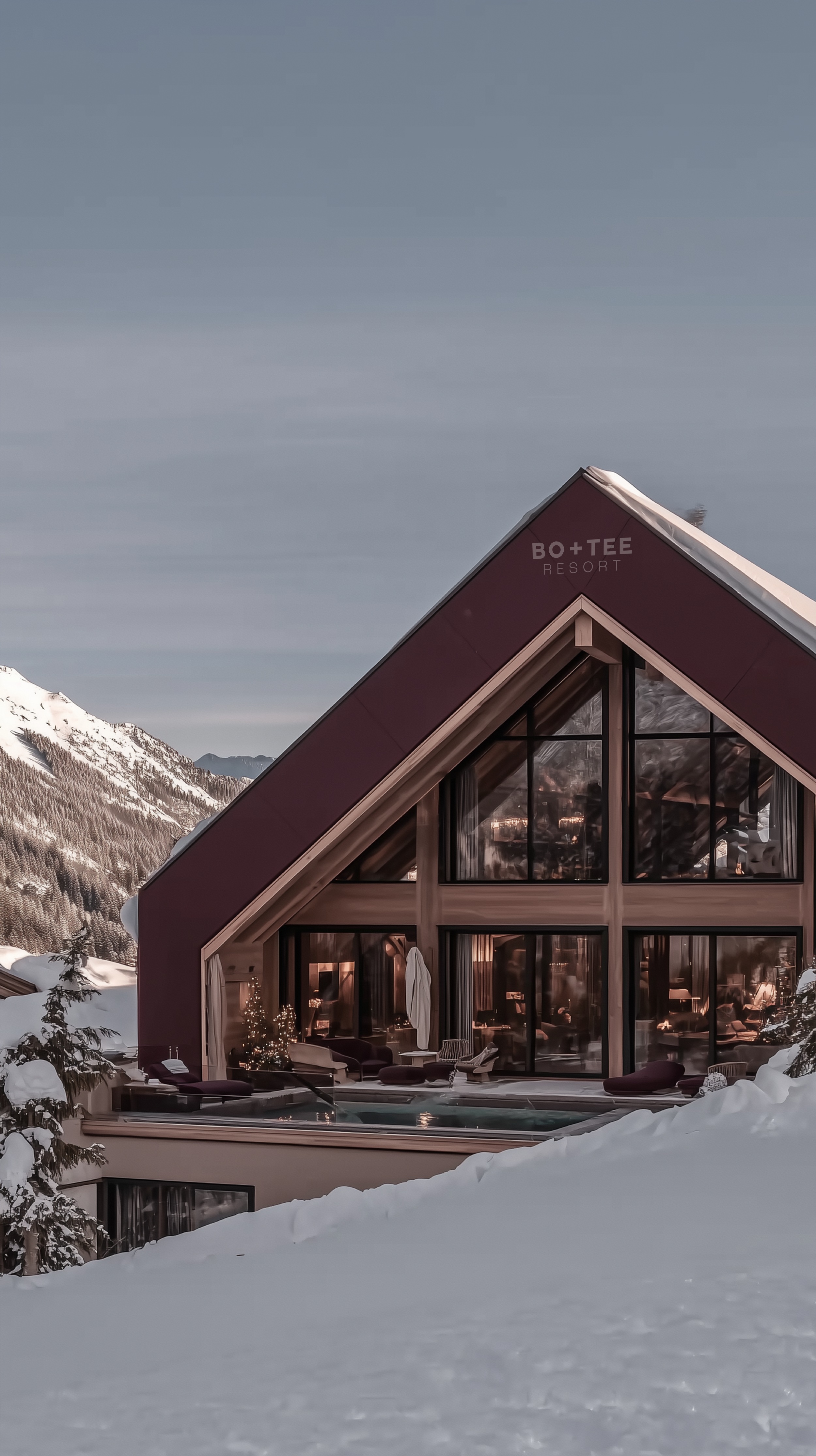 Fictional Bo+Tee ski chalet with a burgundy roof set against snowy mountain peaks